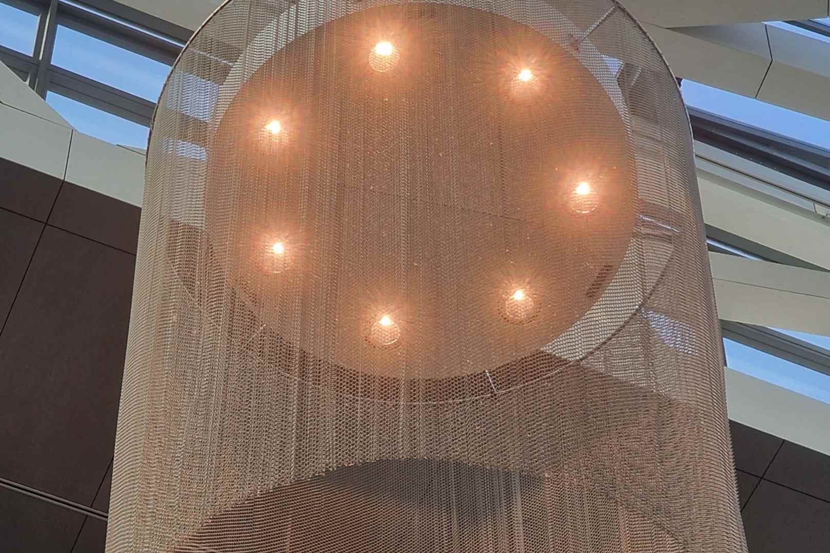 Metalen spiraalgordijn als decoratieve afscherming rond verlichting in een architecturaal interieur
